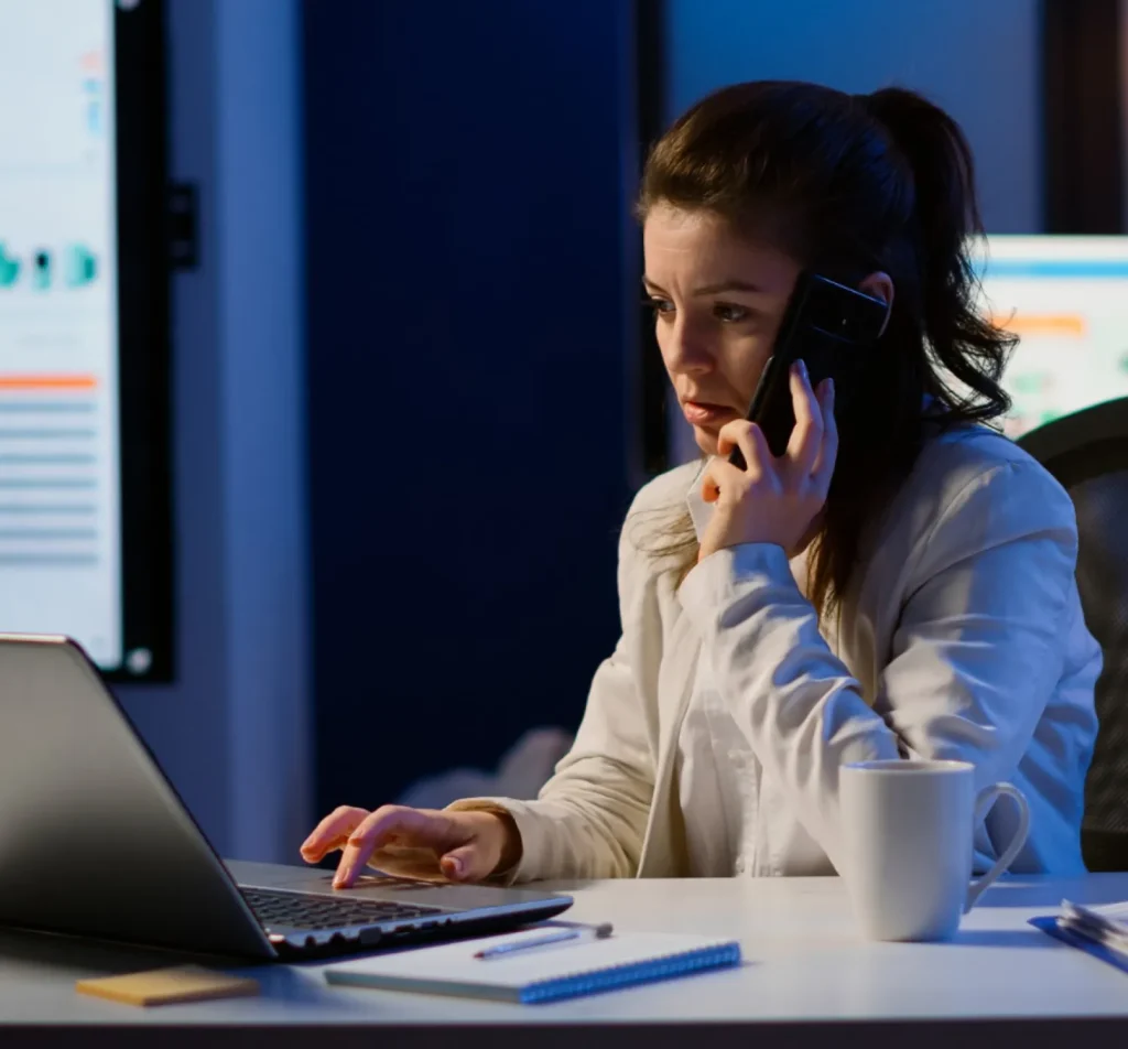 A woman in lab coat looking at a laptop screen while at the same time talking on phone
